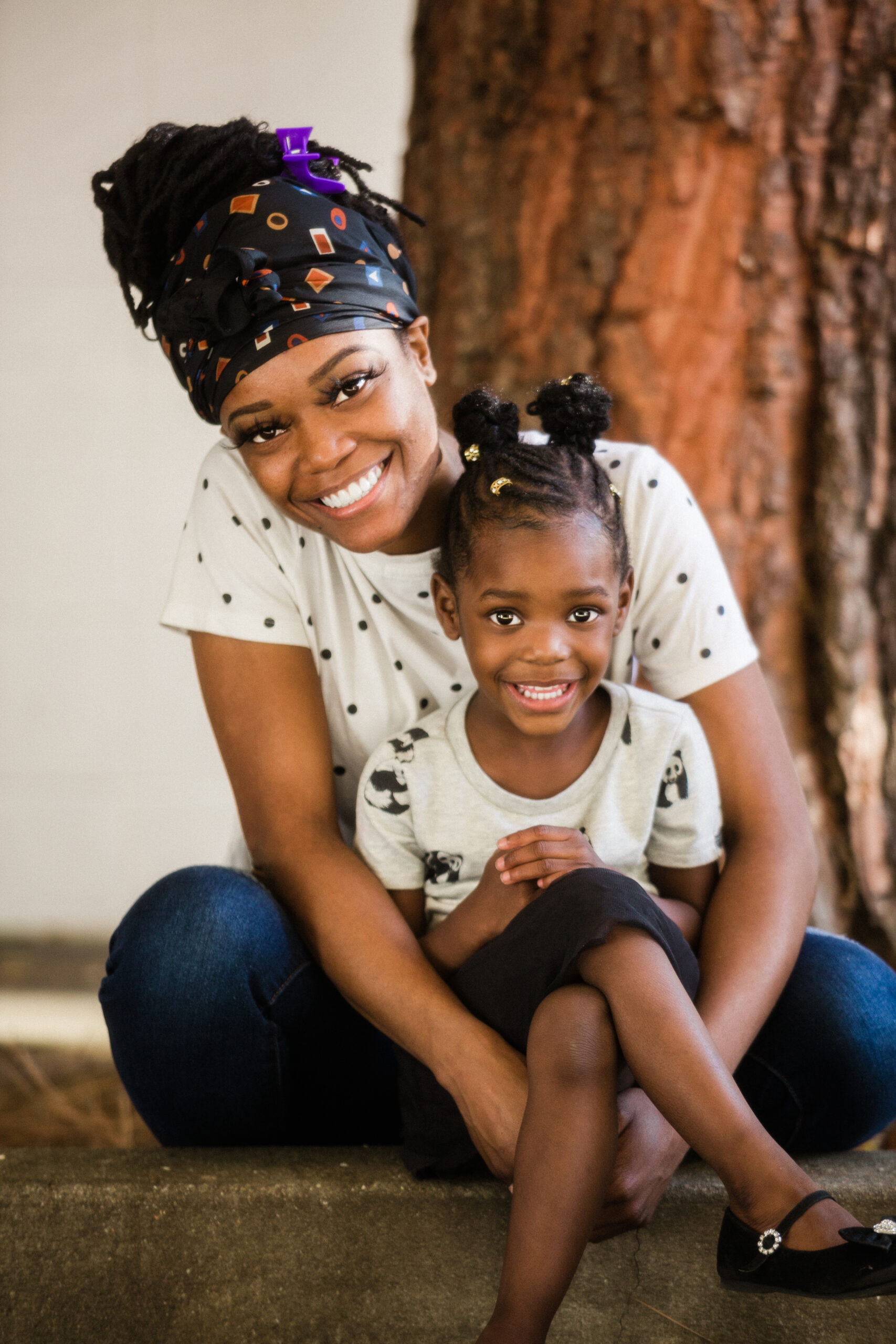 An image of a child and mother sitting together outside with a tree in the background.