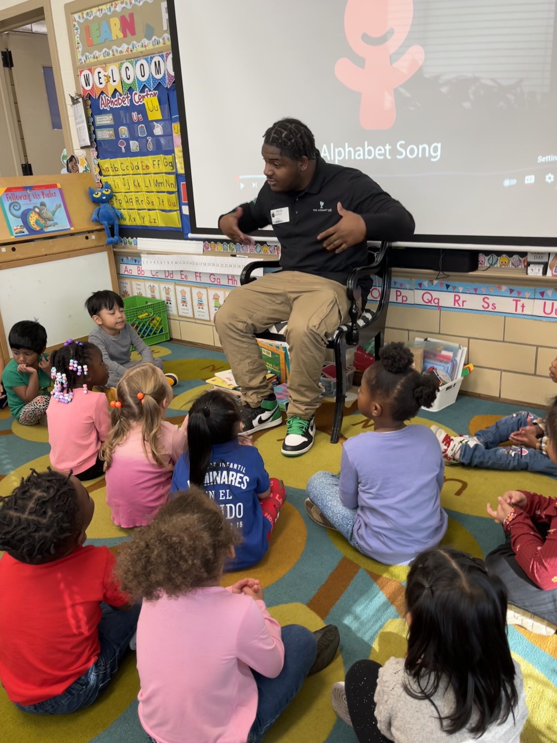 An LMF Fellow surrounded by young students in a classroom singing the alphabet song.