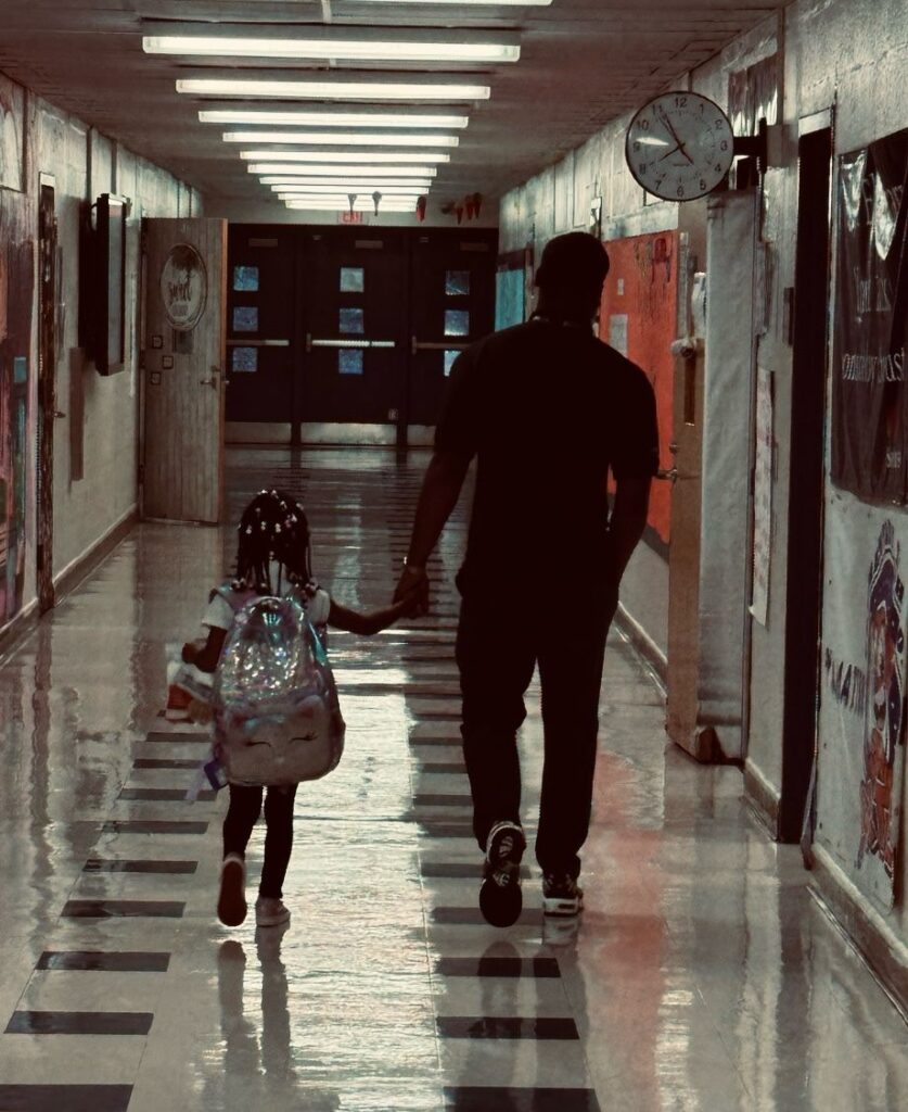 LMF Fellow holding the hand of a young student as they walk down the school hallway.