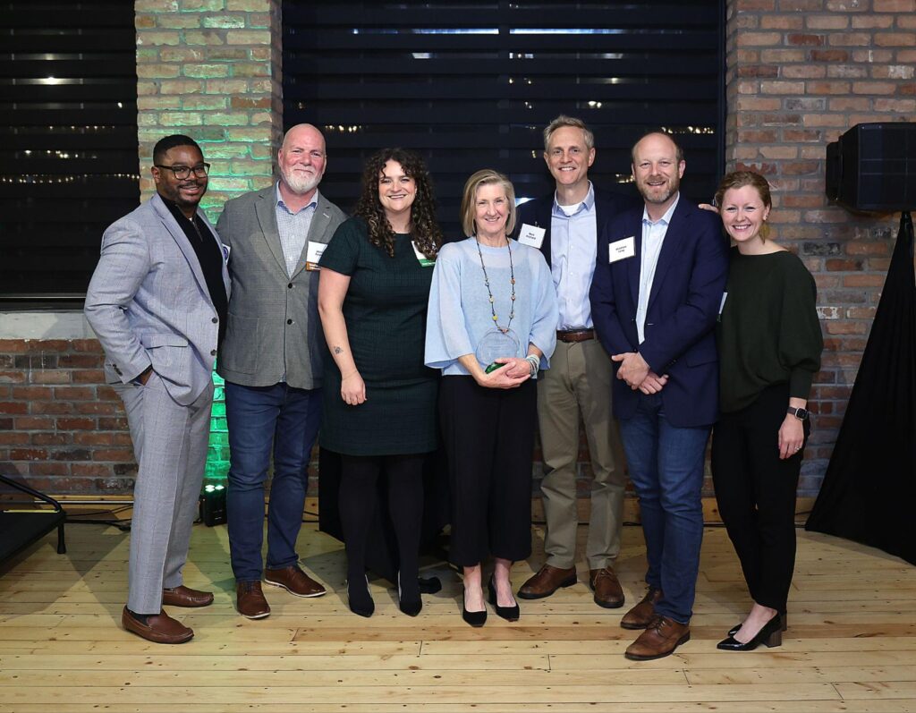 GreenLight staff at the Cinnovation event accompanied by United Way and HomeStart staff members with a brick background highlighted by green lights.