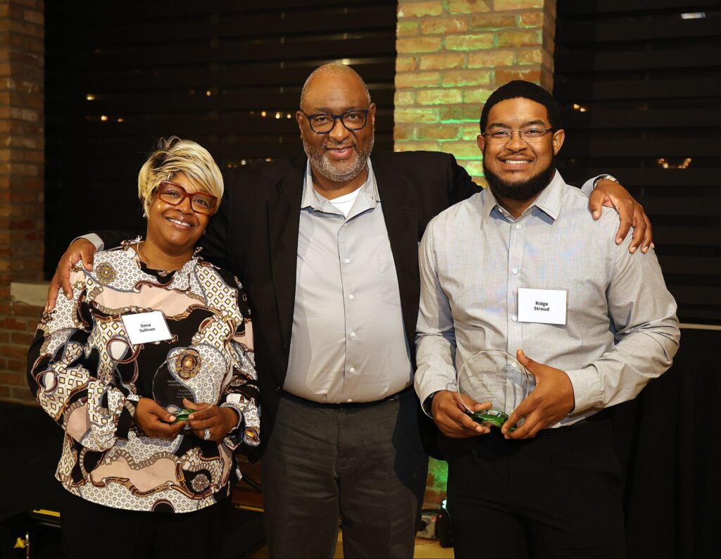 Cincinnati Metropolitan Housing Authority staff gathered together at Cinnovation event with a brick pillar background highlighted by green lights.