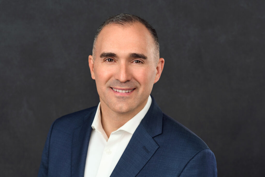 Headshot image of Ryan Friedrichs, a white man with short brown hair wearing a blue blazer over a white button down